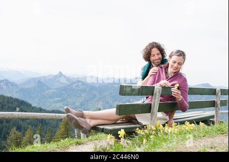 Felice coppia di metà adulto seduta su panchina in montagna contro cielo chiaro Foto Stock