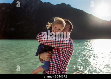 Ragazza allegra che viene portata dal padre contro la montagna e il lago ad Achensee, Stato del Tirolo, Austria Foto Stock