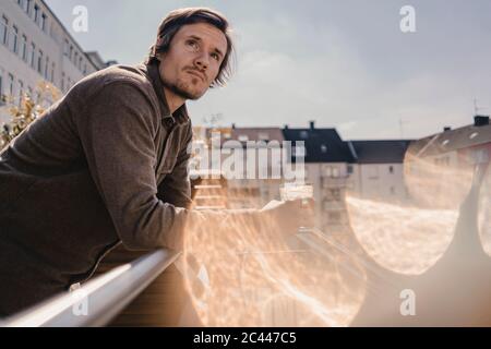 Uomo appoggiato su ringhiera del balcone, con un drink Foto Stock