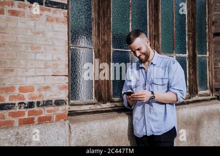 Sorridente giovane uomo guardando il telefono cellulare all'aperto Foto Stock