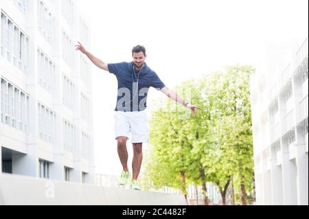 Giovane uomo che si bilancia su un muro in città Foto Stock