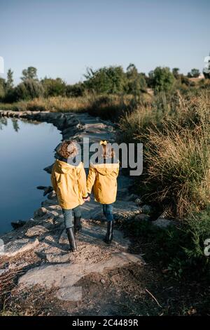 Fratelli che tengono le mani mentre camminano sulle rocce a riva del fiume Foto Stock