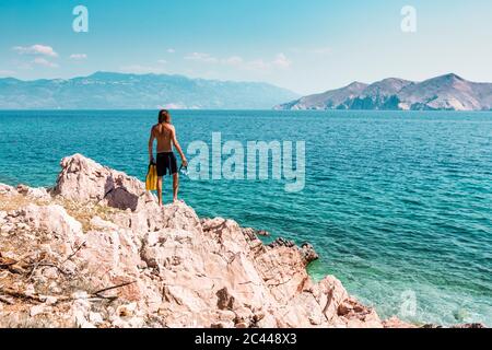 Croazia, Krk, uomo in piedi sulla formazione di roccia e guardando il mare Foto Stock