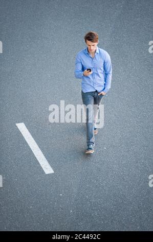 Uomo d'affari che usa lo smartphone mentre cammina sulla strada Foto Stock