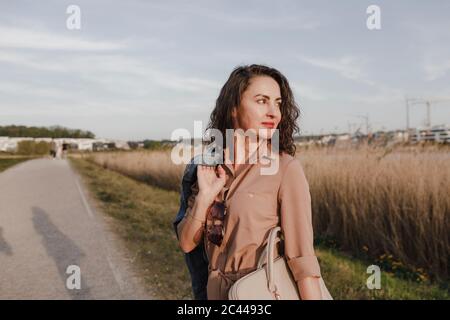 Donna d'affari con cura che trasporta la borsa per il laptop mentre si trova in piedi sul ciglio della strada Foto Stock
