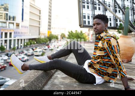 Giovane uomo in camicia a motivi posti sulla terrazza sul tetto della città, Maputo, Mozambico Foto Stock