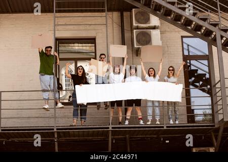 Gruppo eterogeneo di persone che protestano con un cartello bianco. Protesta contro i diritti umani, gli abusi di libertà, le questioni sociali, i problemi reali. Uomini e donne per strada appaiono arrabbiati, urlando. CopySpace. Foto Stock