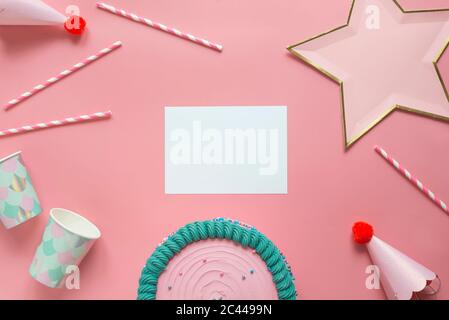 Studio shot di torta di compleanno, pezzo di carta vuoto, cannucce per bere, tazze monouso, cappelli da festa e decorazione a forma di stella Foto Stock