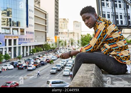 Giovane uomo in camicia a motivi posti sulla terrazza sul tetto della città, Maputo, Mozambico Foto Stock