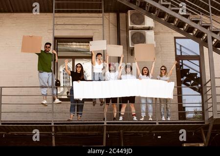 Gruppo eterogeneo di persone che protestano con un cartello bianco. Protesta contro i diritti umani, gli abusi di libertà, le questioni sociali, i problemi reali. Uomini e donne per strada appaiono arrabbiati, urlando. CopySpace. Foto Stock