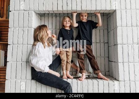 Ritratto di ragazzi in piedi da madre seduto su nicchia bianca a casa Foto Stock