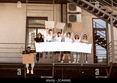 Gruppo eterogeneo di persone che protestano con un cartello bianco. Protesta contro i diritti umani, gli abusi di libertà, le questioni sociali, i problemi reali. Uomini e donne per strada appaiono arrabbiati, urlando. CopySpace. Foto Stock