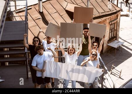 Gruppo eterogeneo di persone che protestano con un cartello bianco. Protesta contro i diritti umani, gli abusi di libertà, le questioni sociali, i problemi reali. Uomini e donne per strada appaiono arrabbiati, urlando. CopySpace. Foto Stock