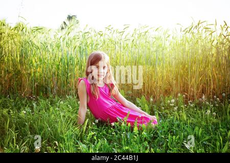 Ritratto di giovane ragazza che indossa vibrante abito rosa seduti nella parte anteriore del campo di segale in estate Foto Stock