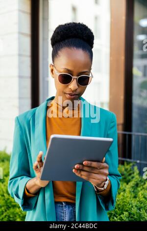 Ritratto di giovane donna d'affari che indossa occhiali da sole utilizzando tablet digitale all'aperto Foto Stock