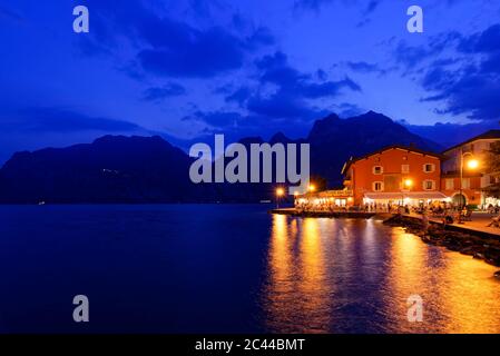 Italia, Trentino, Torbole, Lago di Garda, passeggiata e città illuminate al tramonto Foto Stock