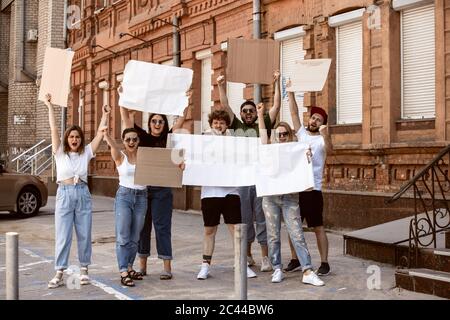 Gruppo eterogeneo di persone che protestano con un cartello bianco. Protesta contro i diritti umani, gli abusi di libertà, le questioni sociali, i problemi reali. Uomini e donne per strada appaiono arrabbiati, urlando. CopySpace. Foto Stock