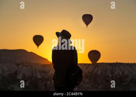 Vista posteriore di silhouette giovane donna guardando i palloni ad aria calda mentre in piedi sulla terra a Goreme, Cappadocia, Turchia Foto Stock