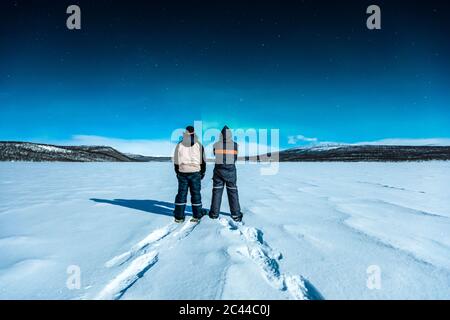 Gli escursionisti con racchette da neve che si trovano nel paesaggio invernale guardando l'aurora settentrionale sopra Ropijarvi, Ropinsalmi, Enontekioe, Finlandia Foto Stock