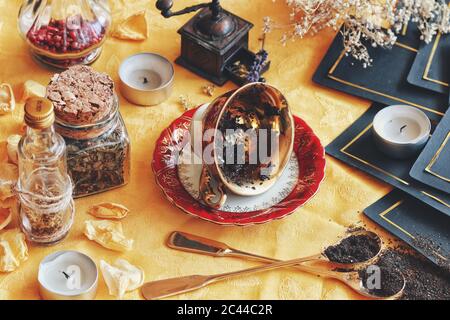 Teacup vintage che si stende sul suo lato su wiccan strega altare per leggere le foglie di tè come un metodo di divinazione per predire il futuro. Panno giallo brillante Foto Stock