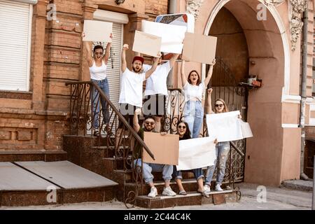 Gruppo eterogeneo di persone che protestano con un cartello bianco. Protesta contro i diritti umani, gli abusi di libertà, le questioni sociali, i problemi reali. Uomini e donne per strada appaiono arrabbiati, urlando. CopySpace. Foto Stock