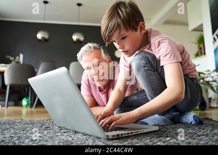 Padre e figlio si stendano sul pavimento, lavorando su un computer portatile Foto Stock