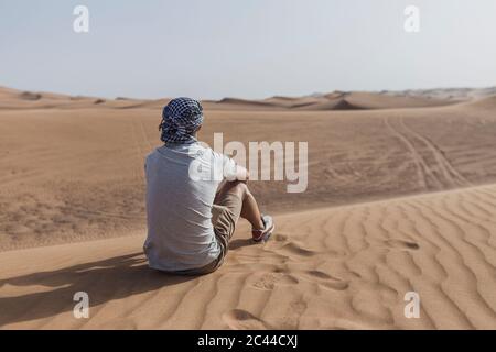 Turista maschile seduto sulle dune di sabbia nel deserto a Dubai, Emirati Arabi Uniti Foto Stock