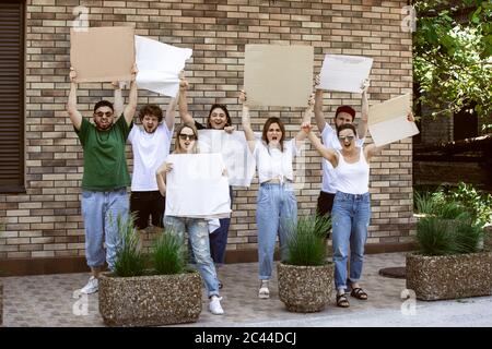 Gruppo eterogeneo di persone che protestano con un cartello bianco. Protesta contro i diritti umani, gli abusi di libertà, le questioni sociali, i problemi reali. Uomini e donne per strada appaiono arrabbiati, urlando. CopySpace. Foto Stock