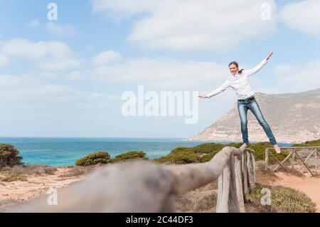 Donna sorridente che si bilancia su recinzione in legno, Sardegna, Italia Foto Stock