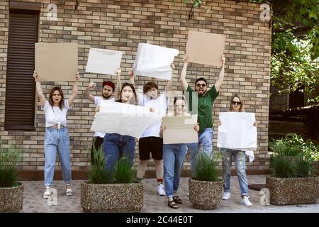 Gruppo eterogeneo di persone che protestano con un cartello bianco. Protesta contro i diritti umani, gli abusi di libertà, le questioni sociali, i problemi reali. Uomini e donne per strada appaiono arrabbiati, urlando. CopySpace. Foto Stock