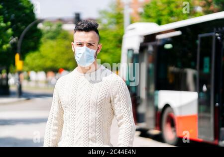 Ritratto di giovane uomo che indossa una maschera protettiva in attesa alla fermata dell'autobus, Spagna Foto Stock