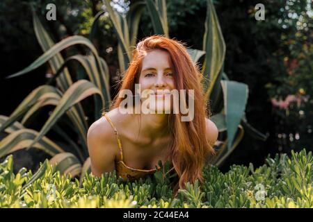 Sorridente giovane bella donna che si appoggia sulle piante in giardino Foto Stock