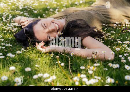 Donna felice godendo il suo tempo libero mentre si sdraiava su erba con margherite Foto Stock