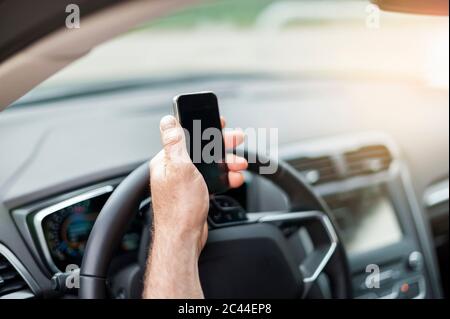Mano tagliata di un uomo che tiene lo smartphone sul volante in auto Foto Stock
