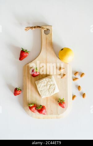 Tagliere in legno, fragole fresche, mandorle, limone singolo e cheesecake vegana fatta in casa Foto Stock