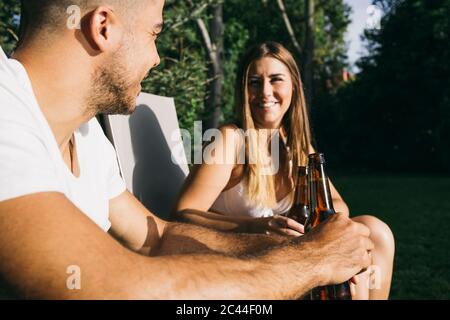 Sorridi una giovane coppia che brinda le bottiglie di birra mentre si siede al resort turistico Foto Stock