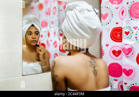 Giovane donna che guarda nello specchio del bagno che applica il trucco Foto Stock