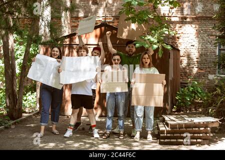 Gruppo eterogeneo di persone che protestano con un cartello bianco. Protesta contro i diritti umani, gli abusi di libertà, le questioni sociali, i problemi reali. Uomini e donne per strada appaiono arrabbiati, urlando. CopySpace. Foto Stock