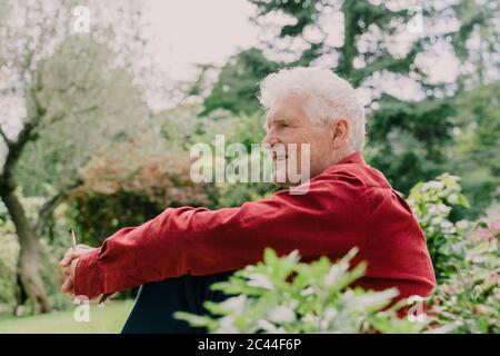 Vista laterale dell'anziano che si rilassa mentre si siede con la marijuana comune al frutteto Foto Stock