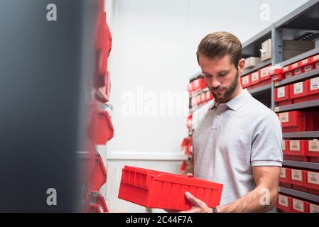 Giovane uomo che tiene una scatola ad un ripiano in una fabbrica Foto Stock