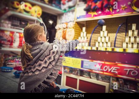 Ragazza giovane in maglione poncho alla cabina giusta che lancia palla mentre si gioca a knockout gioco. Monaco, Germania Foto Stock