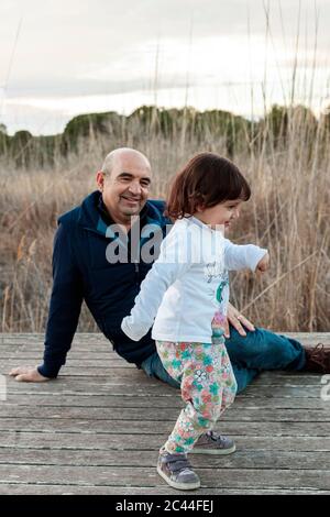 Uomo sorridente che guarda la nipote che gioca sul pavimento Foto Stock