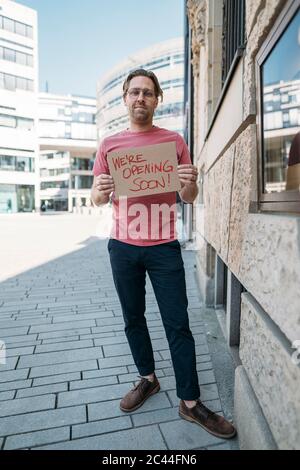 Negoziante in possesso di cartone con annuncio di apertura in città Foto Stock