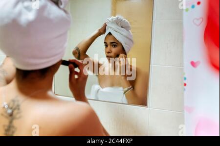 Giovane donna che guarda nello specchio del bagno che applica il trucco Foto Stock