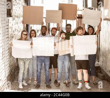 Gruppo eterogeneo di persone che protestano con un cartello bianco. Protesta contro i diritti umani, gli abusi di libertà, le questioni sociali, i problemi reali. Uomini e donne per strada appaiono arrabbiati, urlando. CopySpace. Foto Stock