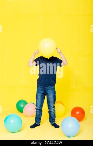 Ragazzo tenendo il palloncino giallo davanti al viso mentre si trova su sfondo colorato Foto Stock
