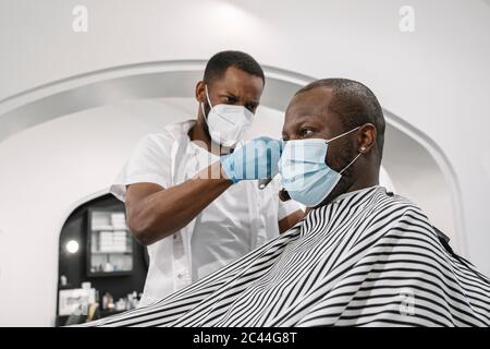 Barbiere indossare maschera chirurgica e guanti tagliando i capelli del cliente Foto Stock