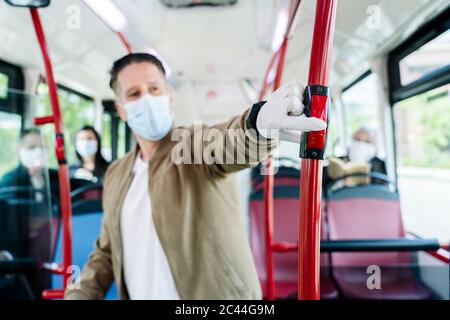 Uomo che indossa maschera protettiva e guanti in autobus pubblico premendo il pulsante di arresto, Spagna Foto Stock