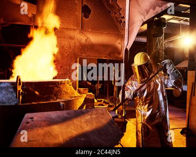 Lavoratore azienda asta metallica in forno alla fonderia Foto Stock