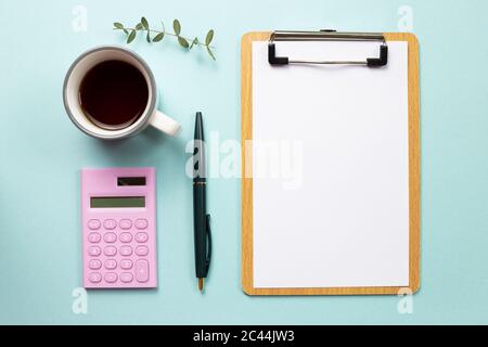 Spazio di lavoro. Appunti e foglio di carta vuoto e calcolatrice con tazza di caffè su sfondo blu. Vista dall'alto Foto Stock